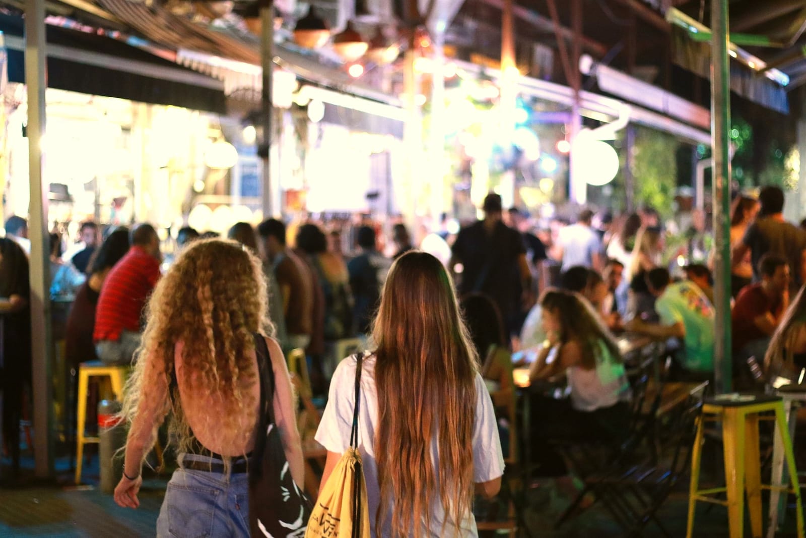 Two friends walking through a lively bar street at night